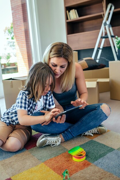 Mère et fils jouant de la tablette assis sur le tapis