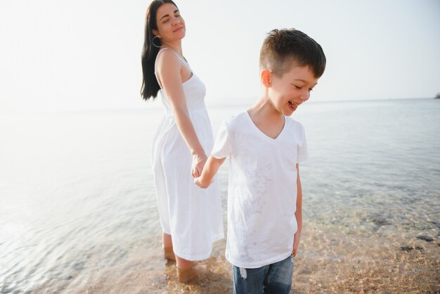 Mère et fils marchant sur la plage au coucher du soleil