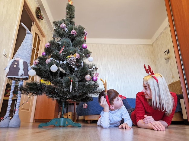 mère et fils, petit garçon s'amusant près de l'arbre de Noël. maison confortable. chandails, cornes de cerf sur la tête