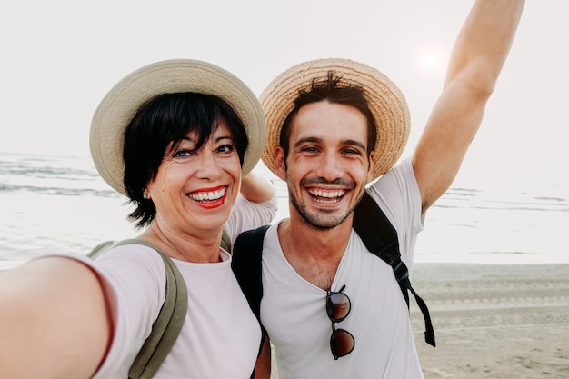 Mère et fils prenant un selfie à la plage avec smartphone.