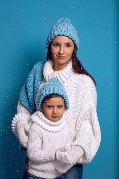 Photo mère et fils en pulls blancs et chapeaux bleus se tiennent sur un fond bleu dans le studio