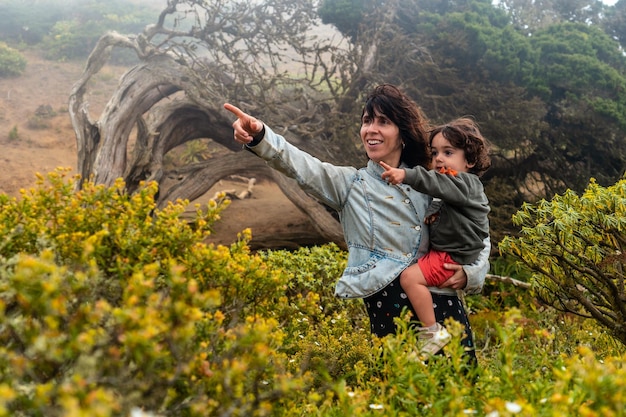 Mère et fils regardant les fleurs à côté d'un arbre Sabinar tordu par le vent d'El Hierro et des îles Canaries brumeuses