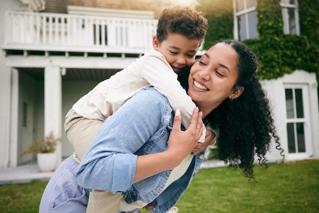 Mère et fils se serrent à dos à l'extérieur avec amour et lien se détendre sur la pelouse de la maison de vacances avec plaisir et bonheur sourire ludique et confiance femme et garçon ensemble dans le jardin avec des vacances et la nature