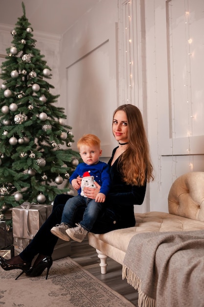 Mère et fils sont assis sur le canapé près du sapin de Noël avec des jouets le jour de l'An