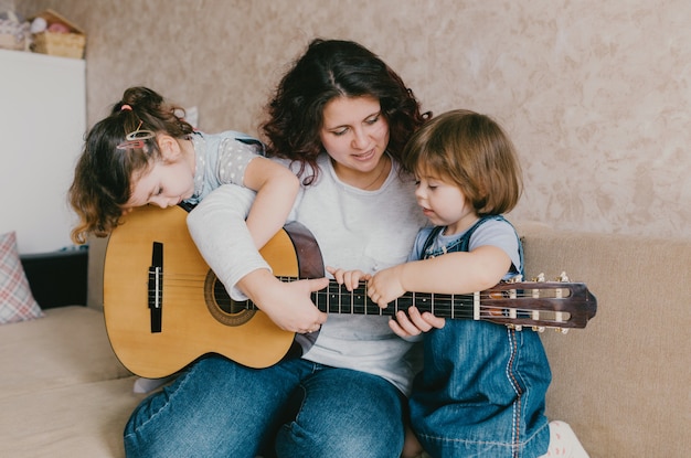 Une mère heureuse apprend à ses deux jeunes filles à jouer de la guitare acoustique.