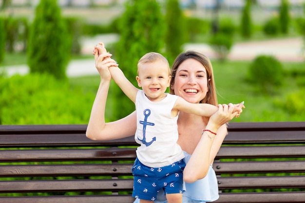 Une mère heureuse avec un bébé dans le parc est assise sur un banc à l'extérieur en plein air et s'amuse avec un bébé dans ses bras