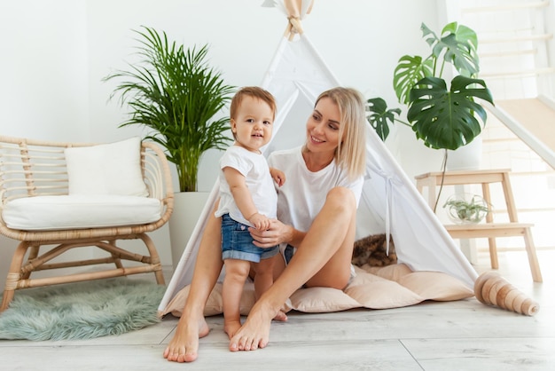 Une mère heureuse et sa petite fille jouent au wigwam à la maison.