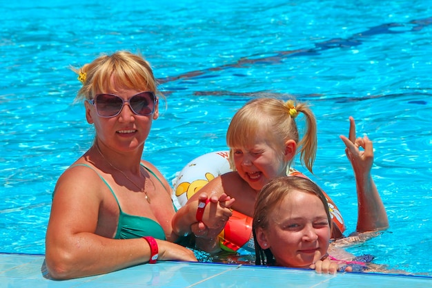 Mère heureuse avec ses filles assises dans la piscine posant devant la caméra Équipe familiale heureuse Famille profitant des vacances d'été Personnes profitant des vacances en famille Équipe féminine