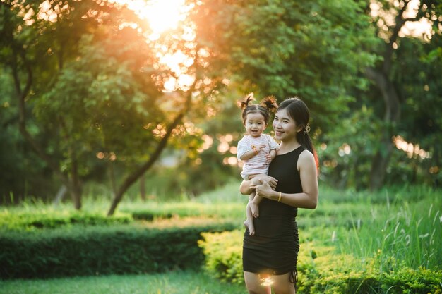 Mère heureuse tenant bébé souriant sur le parc à la lumière du soleil photo en plein air Maman et enfant fille dans la nature Parc en été sur l'herbe verte Concept maman et fille adorable copier l'espace pour le texte