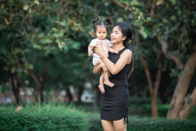 Mère heureuse tenant bébé souriant sur le parc à la lumière du soleil photo en plein air Maman et enfant fille dans la nature Parc en été sur l'herbe verte Concept maman et fille adorable copier l'espace pour le texte