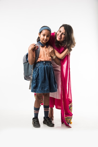 Une mère indienne aide une écolière avec un uniforme à se préparer avec une boîte à lunch, une coiffure ou en attendant le bus scolaire