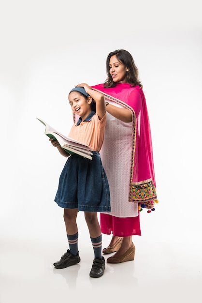 Une mère indienne aide une écolière avec un uniforme à se préparer avec une boîte à lunch, une coiffure ou en attendant le bus scolaire