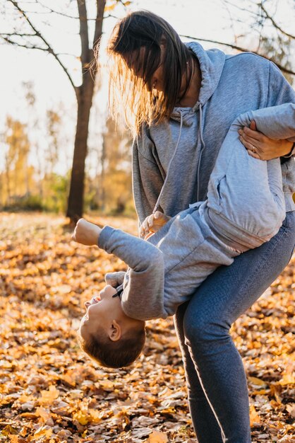 Mère jouant avec son fils à l'extérieur dans le parc le tenant à l'envers souriant enfant heureux