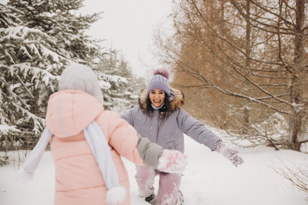 Une mère joyeuse rattrape sa fille, qui court dans la neige de la forêt. promenades d'hiver