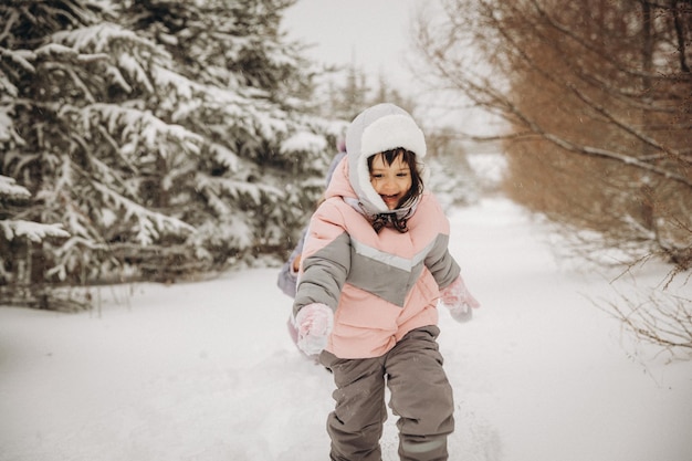 Une mère joyeuse rattrape sa fille, qui court dans la neige de la forêt. promenades d'hiver