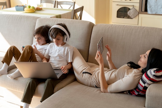 Photo mère et jumeaux utilisant différents appareils à la maison