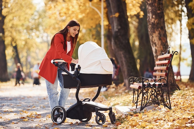 Une mère en manteau rouge se promène avec son enfant dans le landau du parc à l'automne.