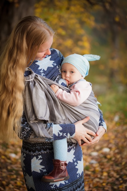 Mère marchant avec enfant en plein air, bébé allaitant en écharpe
