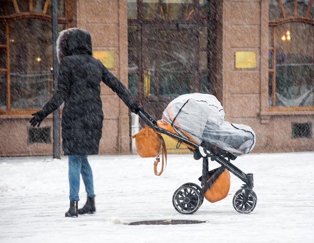 La mère marche avec l'enfant dans la poussette en journée d'hiver enneigée. Flou de mouvement intentionnel. Image défocalisée