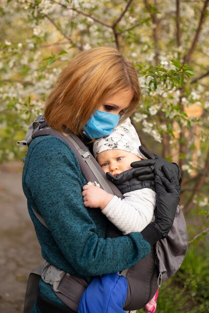 Mère en masque médical avec petit fils dans le parc à pied près de l'arbre en fleurs