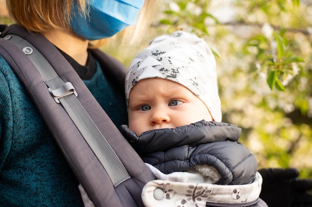 Mère en masque médical et petit fils s'amusent dans les jardins fleuris Portrait femme étreignant petit bébé garçon