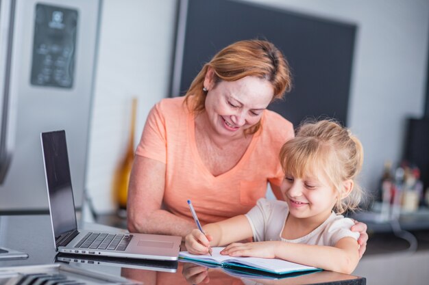 Une mère mature souriante aide sa fille à préparer les tâches ménagères à la maison. Concept d'éducation en ligne.