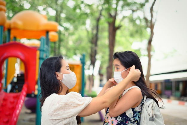 La mère met un masque de sécurité sur le visage de sa fille pour se protéger d'une épidémie de coronavirus dans le parc du village afin de se préparer à aller à l'école. Retour au concept de l'école. Masque médical pour prévenir les coronavirus.