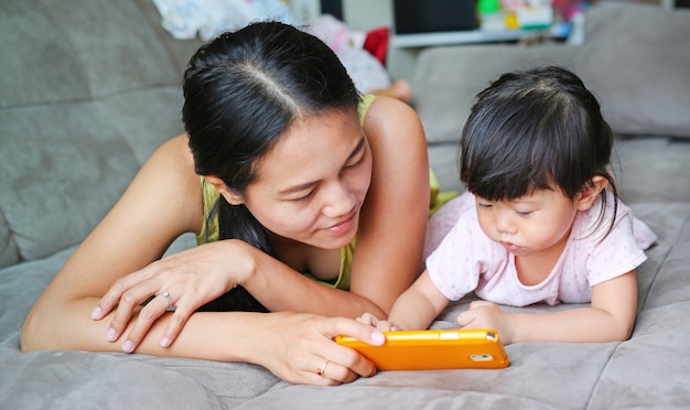 Mère et mignonne asiatique bébé fille jouant un smartphone et la pose