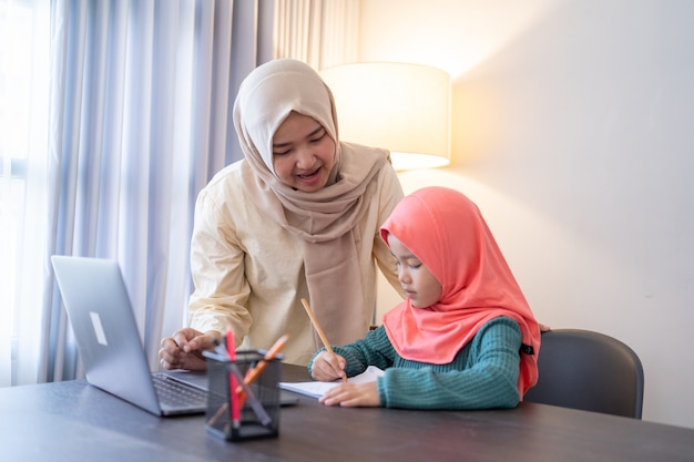 Mère musulmane asiatique aide sa fille à étudier pendant l'enseignement à domicile le soir