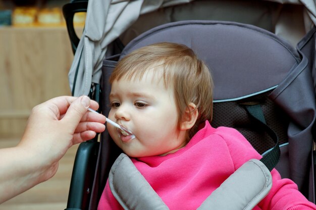 Photo une mère nourrit une petite fille assise dans une poussette avec une cuillère