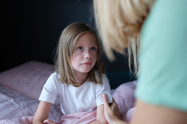 Mère parlant à la petite fille triste au lit