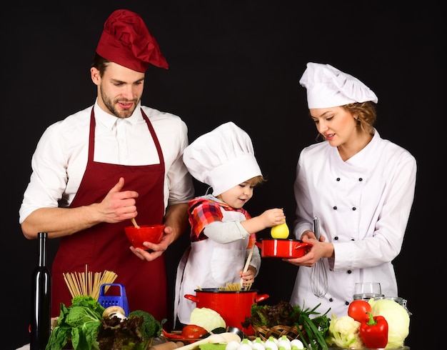 Mère et père apprenant au garçon à cuisiner. Héhé dans la cuisine. L'enfant avec les parents prépare la nourriture.