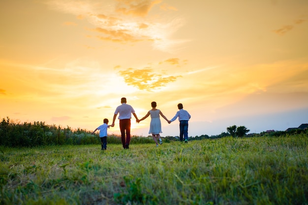 Mère, père et deux fils marchent dans le champ et passent le soleil, vue de dos