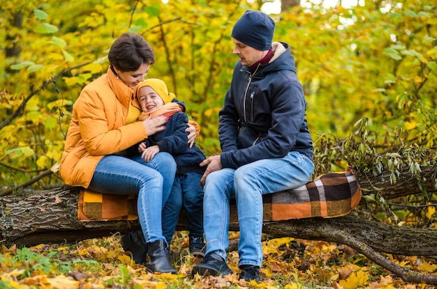 Mère père et petit fils s'assoient sur un plaid sur une bûche dans le parc d'automne et passent du temps ensemble