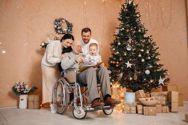 Mère père petit fils et vieux grand-père sur un fauteuil roulant assis près de l'arbre de Noël
