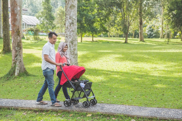 Mère et père poussant la poussette de bébé dans le parc