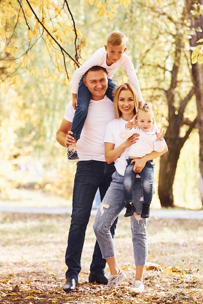 La mère et le père tiennent les enfants sur les épaules et dans les mains. Une jeune famille joyeuse se promène ensemble dans un parc en automne.