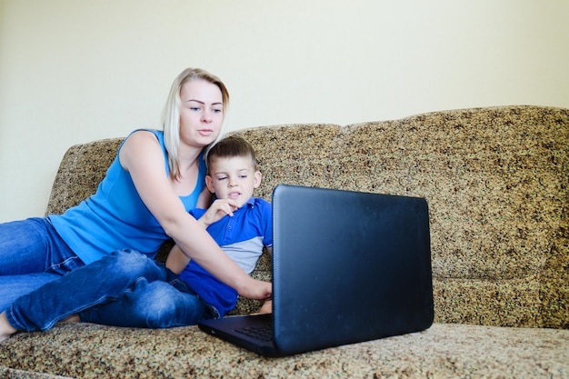 Mère, petit enfant, garçon à la maison assis sur un canapé, détendez-vous. Travail sur ordinateur portable. Shopping en ligne