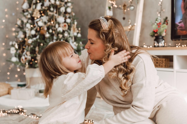 La mère et le petit enfant s'amusent et jouent ensemble à la maison. Une maman joyeuse embrasse une petite fille mignonne près de l'arbre de Noël. Joyeux Noël et bonnes vacances.