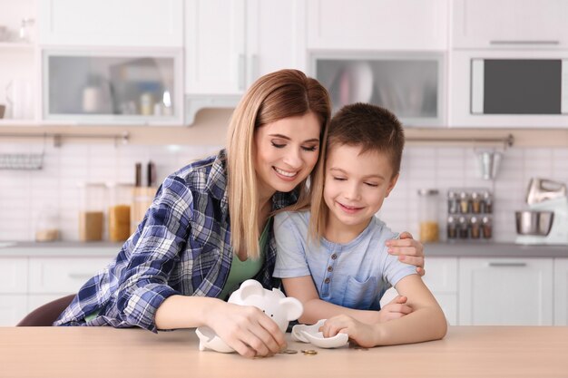 Mère et petit fils avec tirelire cassée sur table à la maison