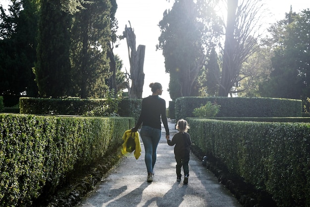 Mère et petite fille en bas âge marchant ensemble sur le chemin au coucher du soleil avec espace de copie Mère et fille marchant sur le sentier à travers un beau jardin Nouvelle protection de la famille et du bébé de maman