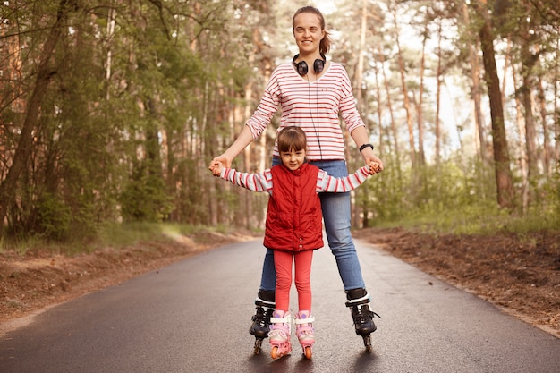 Mère et petite fille charmante jouant dans la forêt, équitation patins à roulettes