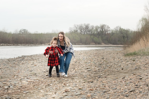 mère et petite fille courent et s'amusent lors d'une promenade à l'extérieur de la ville près de la rivière