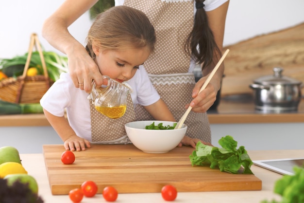 Mère et petite fille cuisinent un délicieux petit déjeuner de salade fraîche Petite aide coupant et mélangeant des tomates et de la verdure Concept de famille heureuse dans la cuisine ou un repas sain