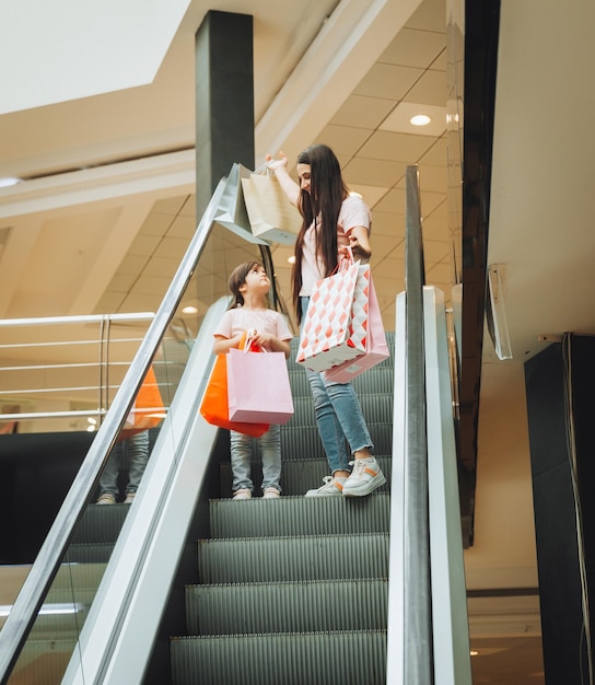 Mère et petite fille sur l'escalator du centre commercialMère et fille du centre commercial Une jeune mère et son petit enfant font leurs courses ensemble