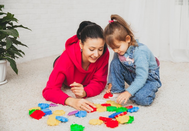 Mère et petite fille jouent au constructeur sur le tapis du salon. famille heureuse