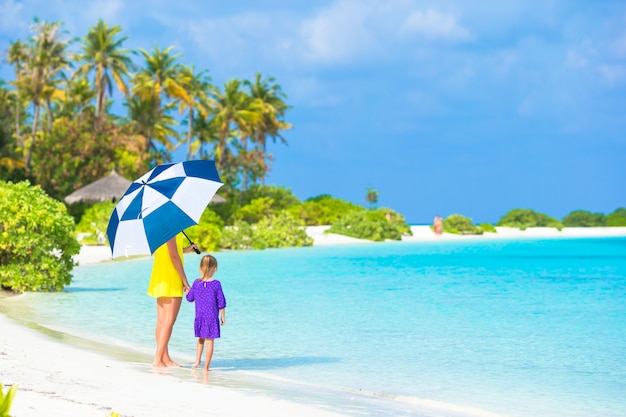 Mère et petite fille avec parapluie se cachant du soleil sur la plage