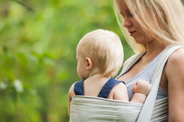 La mère porte son enfant et marche. Bébé en écharpe en plein air.