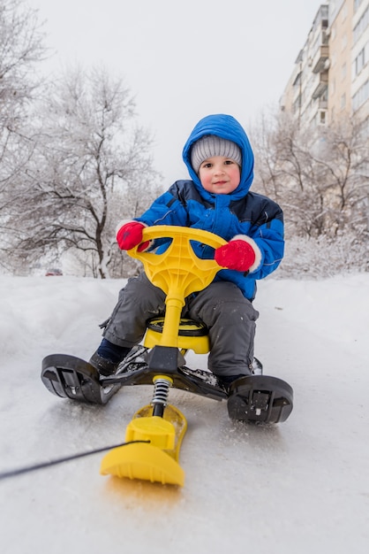 Mère porte son enfant sur une trottinette en hiver