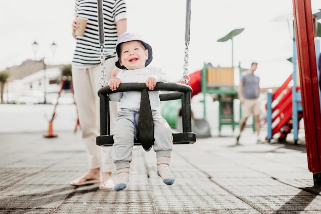 Mère poussant son bébé garçon sur une balançoire sur une aire de jeux à l'extérieur